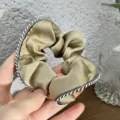 Close-up detail of golden satin hair scrunchie with stylish black white braided edge. - Khaki
