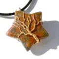 Primo piano di ciondolo in pietra preziosa a stella con disegno dell'albero della vita in filo d'oro. - Unakite