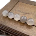 Close-up detail shot of smooth translucent round crystal gemstone beads arranged on wood. - Grey Agate