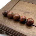 Close-up detail view of 10mm polished red speckled gemstone beads arranged neatly on a wooden tray. - Mahogany Obsidian