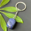 Detail shot of polished blue crystal gemstone keychain with stainless steel ring and green leaf decor. - 15-20mm Tumbled Stone / Sodalite Keychain