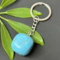 Detailed close-up of a vibrant blue tumbled gemstone keychain on green leaves and dark background. - 15-20mm Tumbled Stone / Synthetic Turquoise Keychain