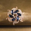 Elegant flower brooch detail featuring rose gold metal and sparkling blue and clear crystals. - Blue