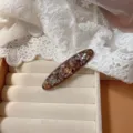 Primer plano detallado del elegante pasador de pelo de pedrería con cristales brillantes. - Pieza Única / Marrón