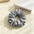 Close-up detail of a soft gray fabric hair scrunchie with neat stitching and chic label accent. - Gray