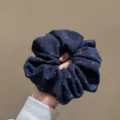 Gros plan d'un chouchou en tissu bleu foncé à pois blancs, accessoire élastique pour cheveux. - Bleu marine