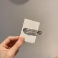 Gros plan detaille d une epingle a cheveux en metal argente sur une carte blanche. - Carré / Argent