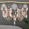 Handmade dream catcher detail showing lace crochet, pink feathers, and rustic hanging branch. - Pink