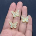 Detail view of miniature yellow resin butterfly DIY charms shown on hand palm for handmade jewelry crafting. - 14x19mm 670 Pieces / Yellow