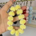 Close-up detail of fluffy pom pom and faux pearl wrist strap keychain, soft plush texture. - Yellow