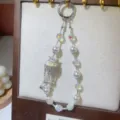 Close-up detail of luxury crystal pearl beaded wrist strap and charming phone charm pendant. - White