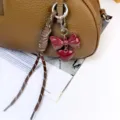 Detailed shot of a brown leather bag with a glossy burgundy bow heart keychain pendant. - Angola Red