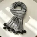 Grey knit winter scarf detail with cute pom pom accents, cozy warm fabric texture. - Light Gray
