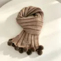 Dettaglio della sciarpa in maglia con morbida struttura in lana, design a costole e pon pon. - Cachi
