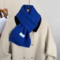 Primo piano della sciarpa in maglia blu accogliente sul cappotto, consistenza morbida. - Blu Zaffiro