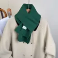 Dettaglio della sciarpa in maglia verde scuro su cappotto beige, morbida ideale per inverno. - Verde Marte