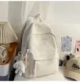 Vue détaillée du sac à dos blanc minimaliste brodé, avec de jolis nœuds et un pendant. - Grand (Avec Pendentif) / Blanc