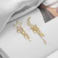 Asymmetrical celestial star and moon tassel earrings, detailed close-up shot of gold plated design. - Moon and Star Tassel Earrings