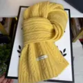 Close-up detail of a cozy yellow cable knit wool blend winter scarf with brand tag. - Milk Yellow