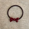 Dettaglio in primo piano dell'elastico marrone scuro con fiocco in acetato bordeaux lucido. - Nastro Rosso