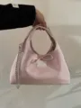 Pink glossy handbag detail showing metal chain strap and cute front bow patch decoration. - Pink