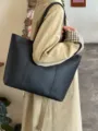Detailed shot of a stylish black PU leather tote bag worn on shoulder for daily commute. - Black