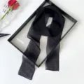 Black sheer long scarf detail shot, elegant thin ribbon accessory displayed on a chic tray. - Black