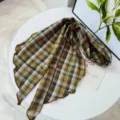 Detailed shot of a vintage plaid ribbon scarf with lettuce edge on a white tabletop. - Long Rhombus Scarf / Coffee and Rice Plaid