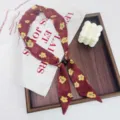 Close-up detail of the retro floral skinny scarf with black bead accent on wooden tray. - Yellow Small Floral Brown Base