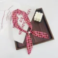Close-up detail of vintage pink floral ribbon scarf with pearl pendant displayed on tray. - Pink Small Floral Pink Base