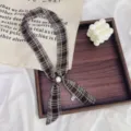 Detailed view of the vintage brown plaid skinny scarf with a pearl buckle ornament. - Green Line Brown Plaid White Bead