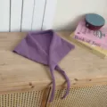 Detail shot of a purple knitted triangular scarf with thin ties, displayed on a wooden table. - Taro Purple