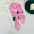 Dettaglio di un foulard quadrato in seta rosa chiaro, accessorio elegante e leggero. - Rosa
