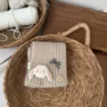Detailansicht des niedlichen Strickschals für Kinder mit Plüschhasen und Karoschleife. - Gebrochenes Weiß