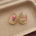 Detail shot of oval resin earrings featuring natural dried flowers and elegant gold metal rims. - Oval Flowers