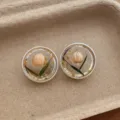 Close-up detail of clear resin stud earrings featuring embedded dry flower buds and gold foil. - Round Flower