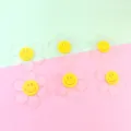 Clear glitter acrylic flower pendants with yellow smiley face center detail view. - 55mm