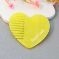 Close-up of yellow acrylic heart-shaped comb detail with hole and Good Luck letter print design. - Yellow