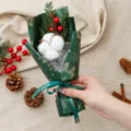 Close-up shot of a Christmas dried cotton flower bouquet with red berries and ribbon detail. - Cotton Green Christmas Bouquet