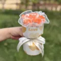 Detail shot of artificial soap rose bouquet in gift wrapping with love text and ribbon. - Sunset Orange