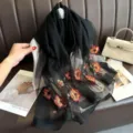 Exquisite black sheer silk scarf featuring vibrant red and yellow floral embroidery details. - Black