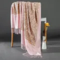 Close-up view of a pink cashmere-feel shawl with golden paisley embroidery and stylish fringe. - Pink