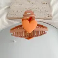 Detailed closeup of a cute macaron orange heart hair claw clip, stylish back hair shark clip. - Orange