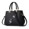 Vista dettagliata della borsa in pelle nera con ricamo floreale delicato e dettagli metallici. - Nero