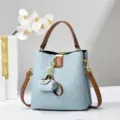 Vista dettagliata della elegante borsa a secchiello blu con manici marroni e grazioso ciondolo. - Blu