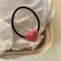 Detalle en primer plano del bonito coletero de pelo con corazón rosa y acabado brillante. - Rosa