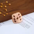 Close-up detail of handmade wool felt square cookie charm with brown spots on book page. - Sesame Bread Basket