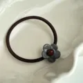Vista detallada de la bonita goma de pelo pequeña de flor con perla roja brillante. - Gris