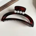 Vista detallada de una pinza para el cabello en forma de media luna marrón con perlas. - Ámbar Mate