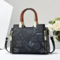 Elegante borsa da donna nera con stampa di lettere, manico in ambra e dettagli dorati. - Nero